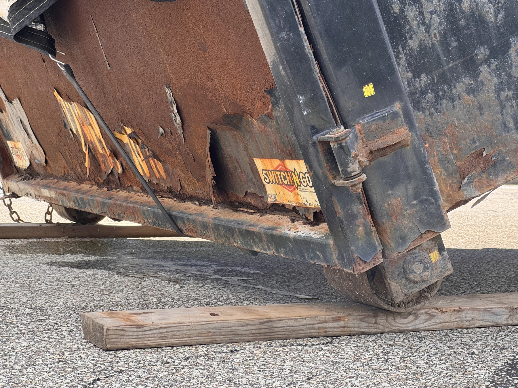 Dumpster wheel resting on a wooden board over pavement