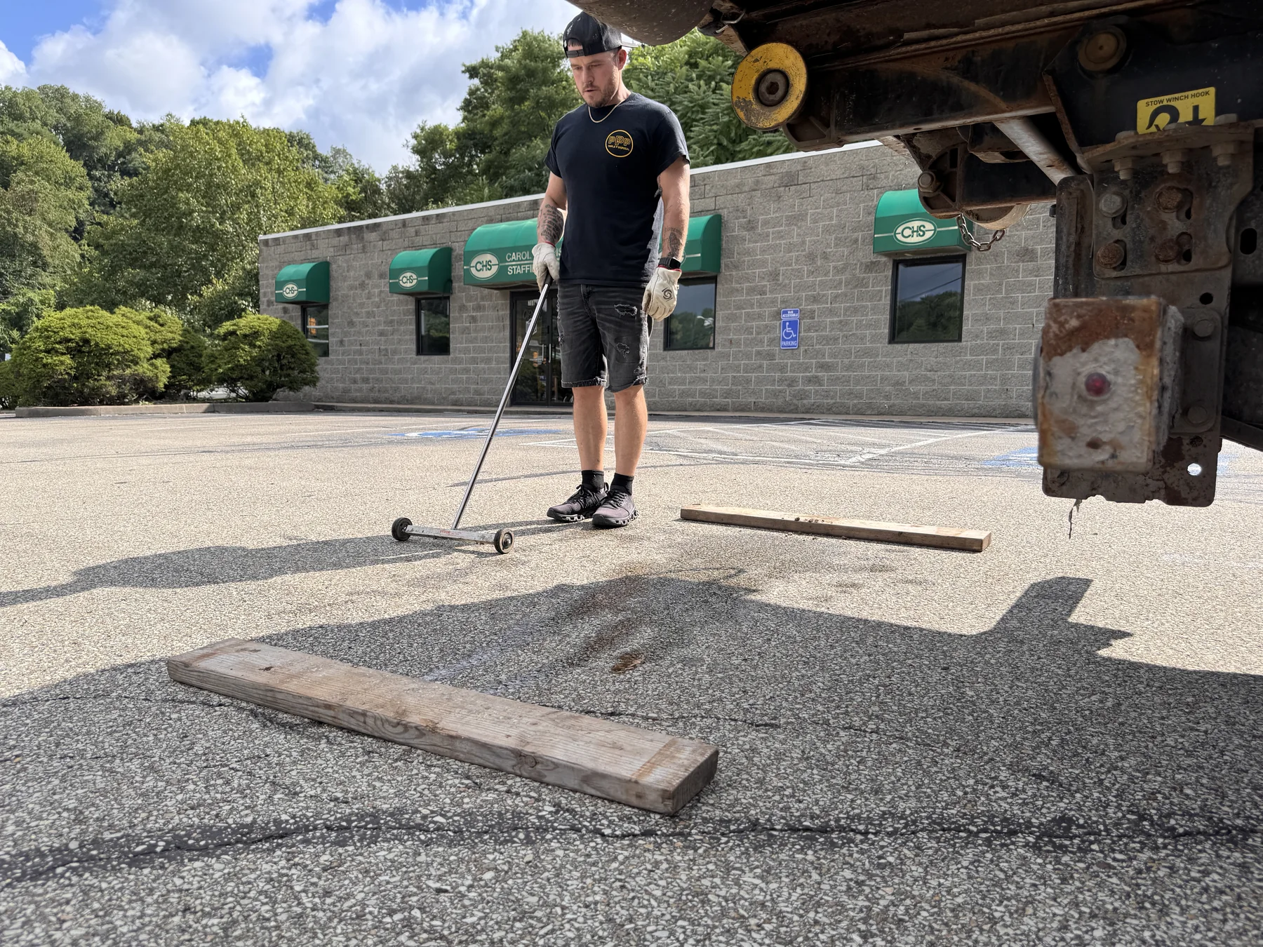 Triple P worker using a rolling magnet beside a dumpster set on wooden boards
